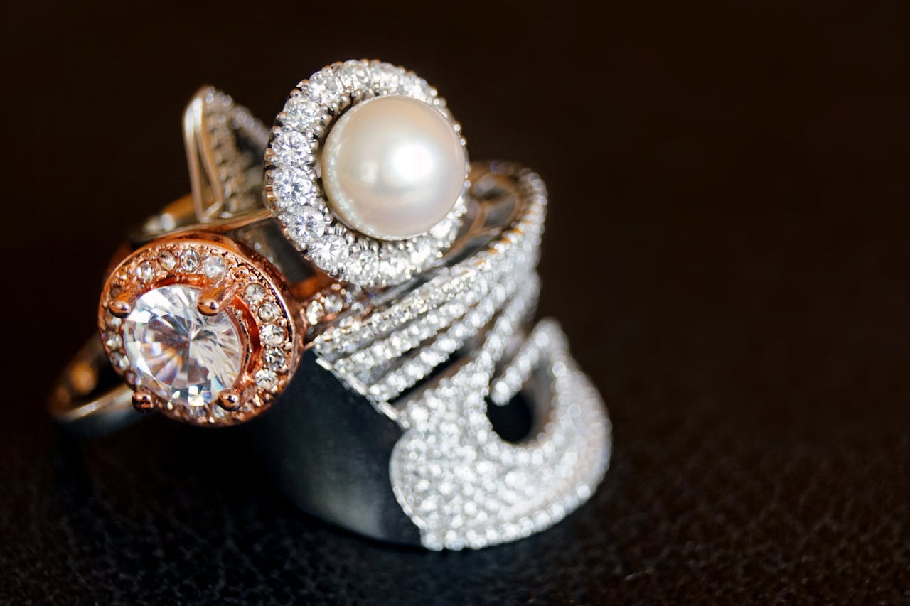 Close-up of luxurious pearl and diamond rings with gold accents on a black background.