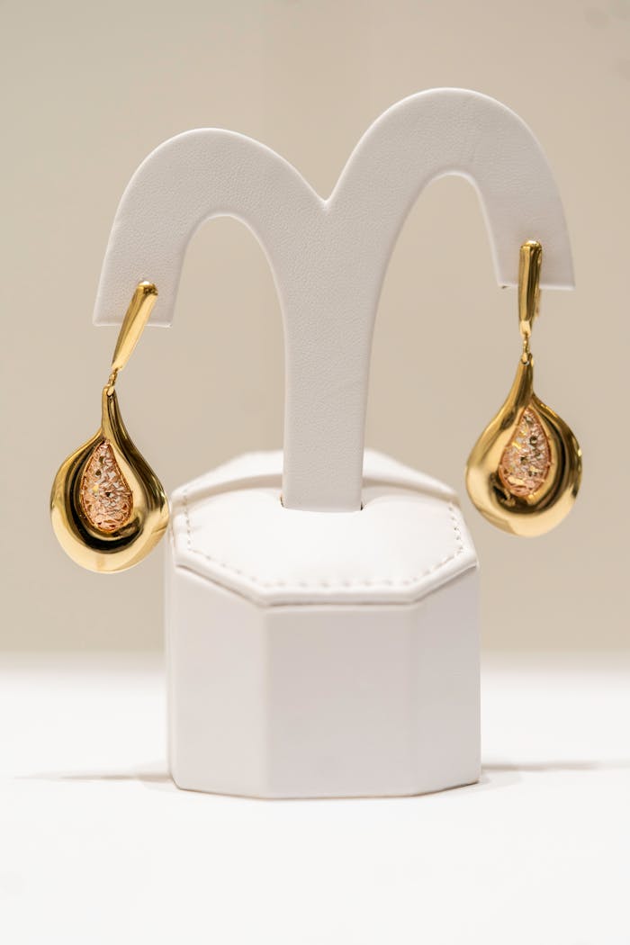 gallery-5 Luxurious gold earrings beautifully displayed on a white stand in a well-lit environment.